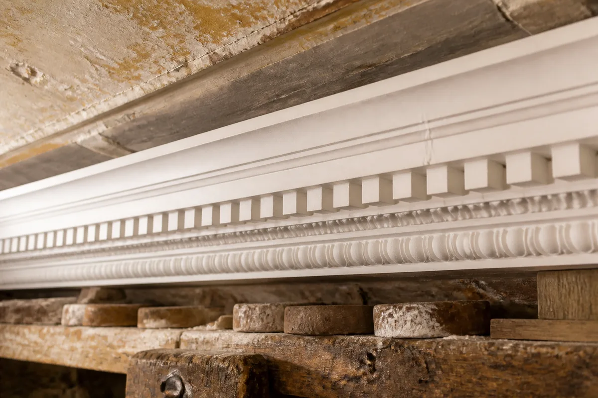 Détail d’une corniche en staff avec denticules et arête vive sous un plafond ancien